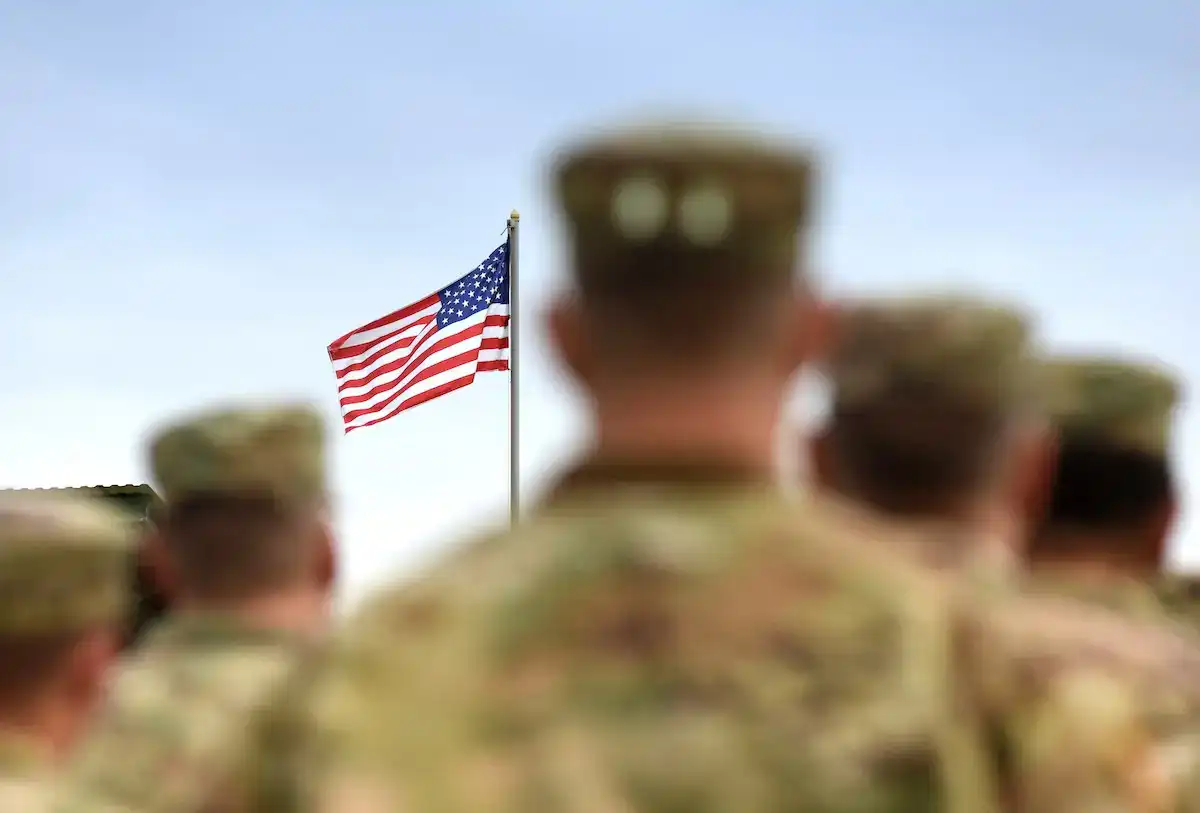 American soldiers in uniform saluting at the flagpole.