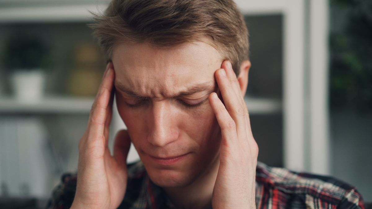 A person at a computer rubbing their temples with a worried, tired expression