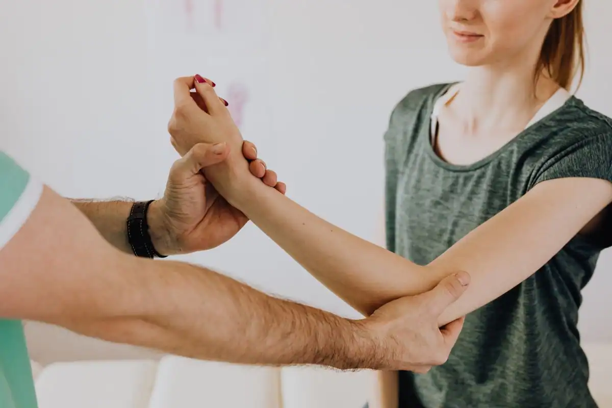 A chiropractor examining the arm and shoulder of a smiling female patient in a clinic