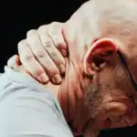 A man gripping the side of his stiff neck in visible discomfort