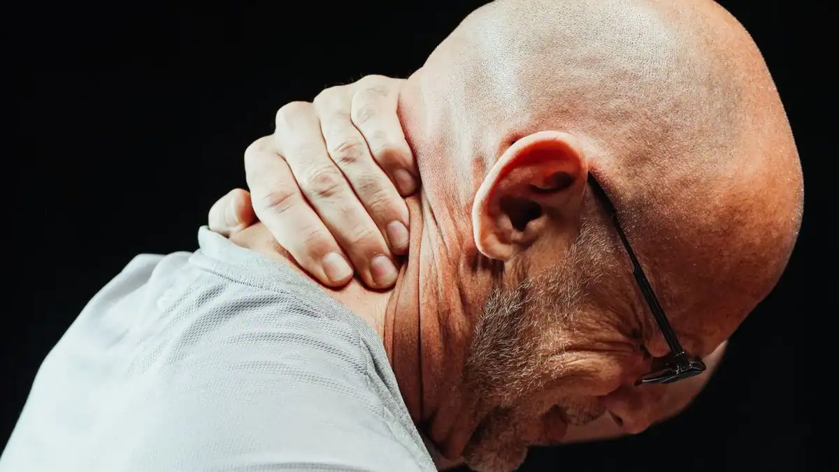 A man gripping the side of his stiff neck in visible discomfort