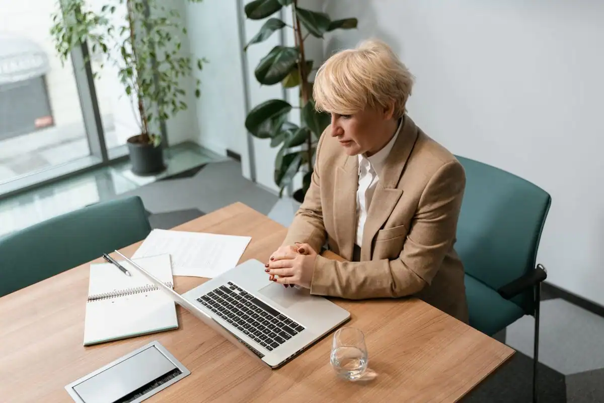 A woman sitting at a desk leaning toward her computer screen with rounded shoulders
