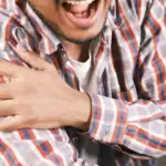 A man holding his aching left shoulder with his opposite hand