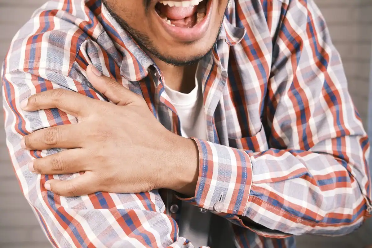 A man holding his aching left shoulder with his opposite hand
