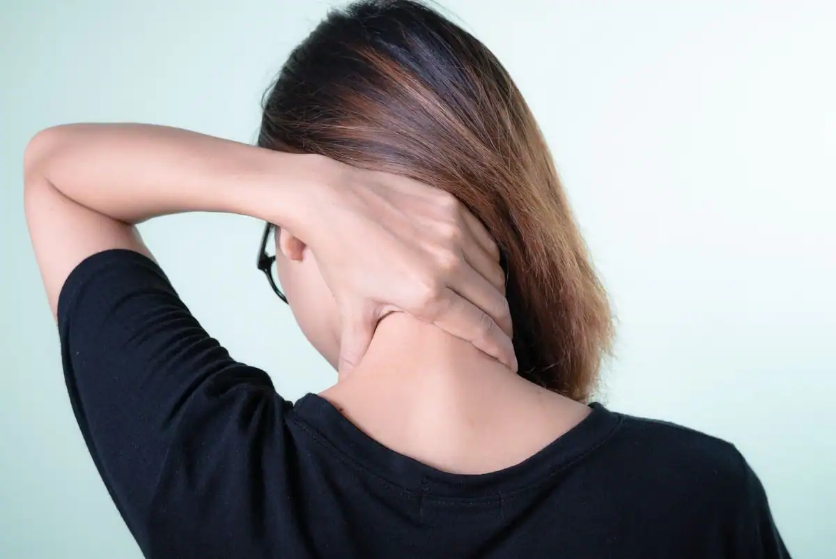 A woman seen from behind massaging her sore neck with both hands