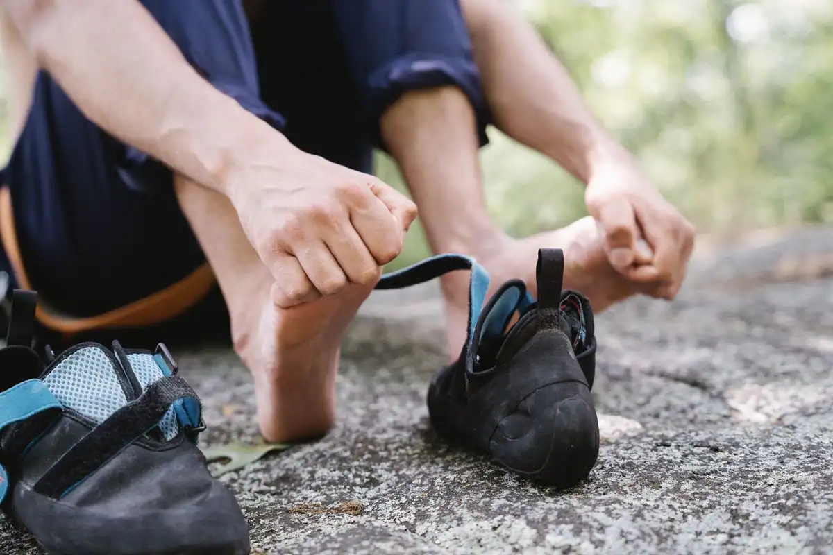 A barefoot person seated on a rock outdoors pulling on snug athletic shoes