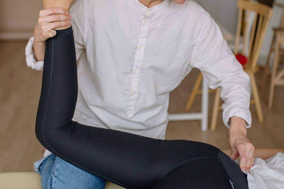 A therapist bending a patient's leg at the knee and hip while steadying the pelvis to check hip mobility
