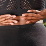 Close-up of a woman pressing both hands against her lower back, a common sign of back pain that ice or heat may help ease