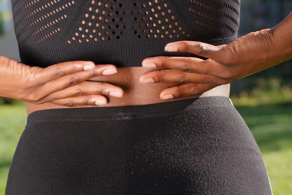 Close-up of a woman pressing both hands against her lower back, a common sign of back pain that ice or heat may help ease